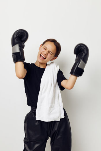 Portrait of young woman lifting dumbbell while standing against white background