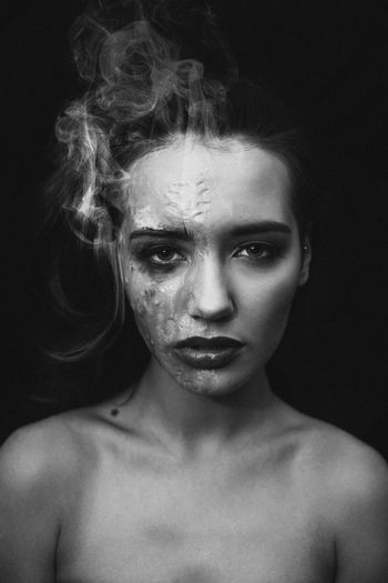 Close-up portrait of topless woman with burnt face against black background