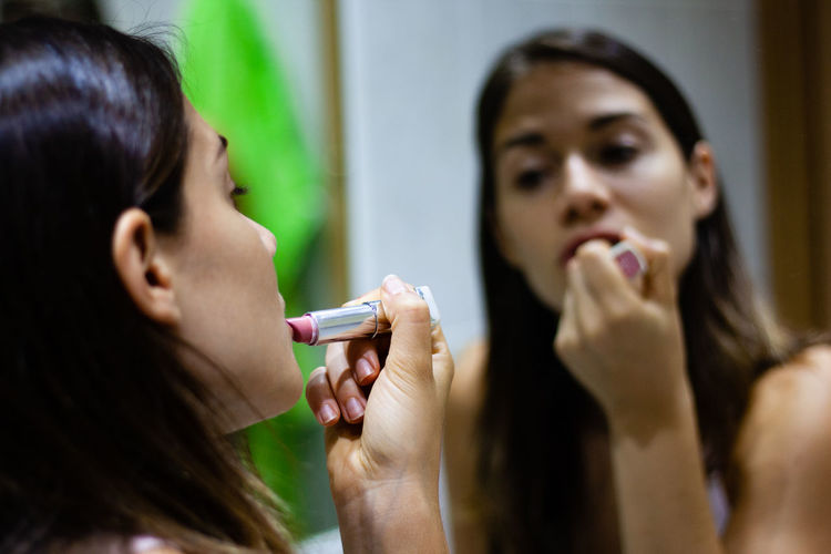 Close-up of woman applying lipstick against mirror