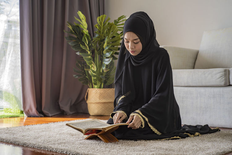 Young woman reading koran while sitting on floor at home