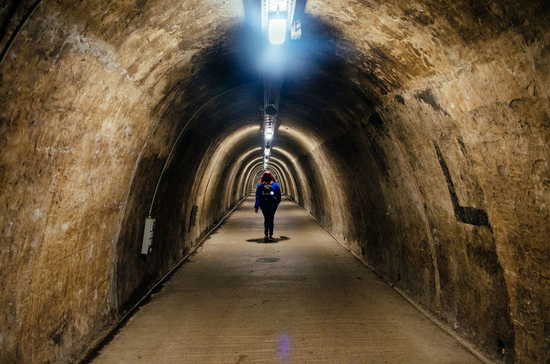 Rear view of man walking in illuminated tunnel