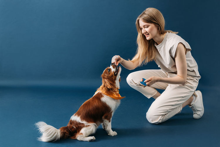 Side view of young woman with dog against blue background