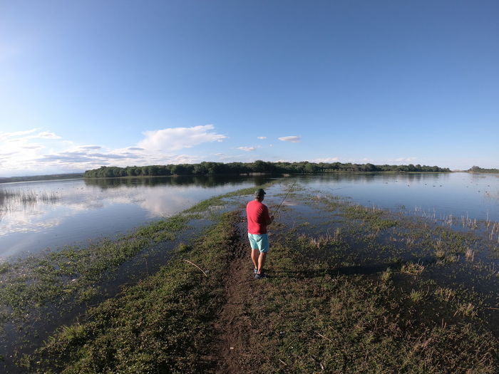Rear view of man looking at lake against sky