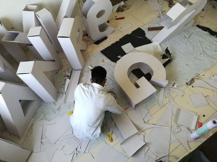 High angle view of man making alphabets with cardboard in workshop