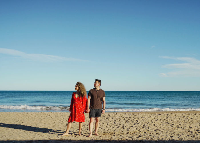 Rear view of woman and man in love standing at beach against sky