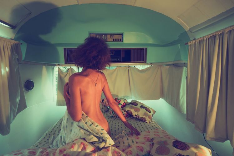 Rear view of naked woman sitting on bed in travel trailer