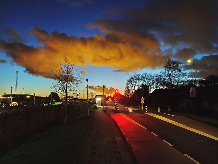 Road by illuminated city against sky at sunset
