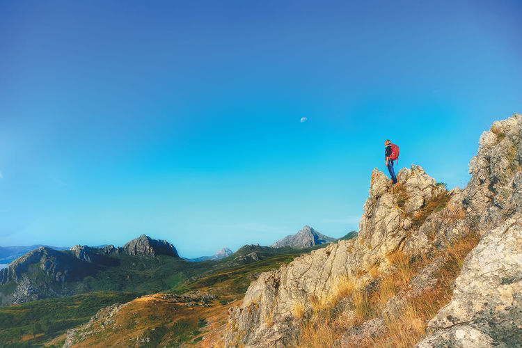 Mature woman standing on mountain against blue sky