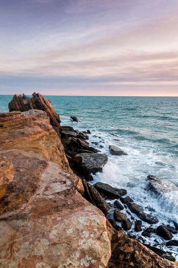 Scenic view of rock by sea against sky during sunset