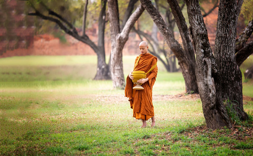 Monk carrying container while standing on land