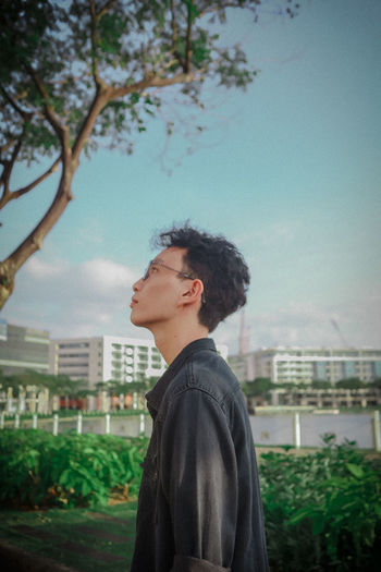 Side view of young man looking at camera against sky