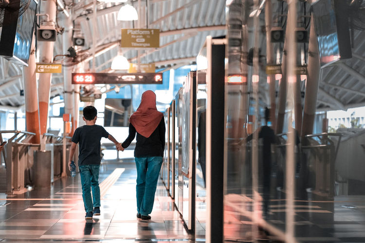 Rear view of siblings walking on subway station in city