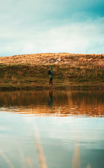 Reflection of man in lake against sky
