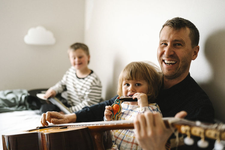 Portrait of happy father with guitar and daughter sitting in bedroom