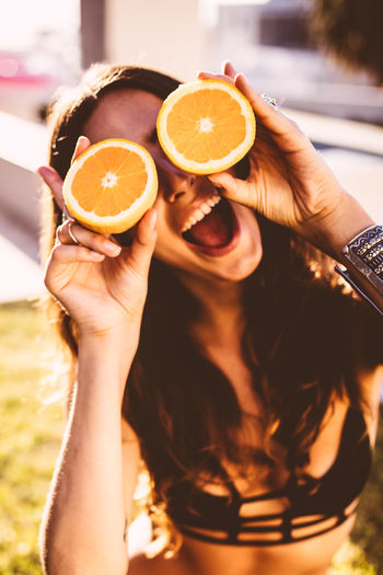 Cheerful woman covering her eyes with sliced oranges