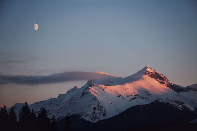 Scenic view of snowcapped mountains and moon during sunset