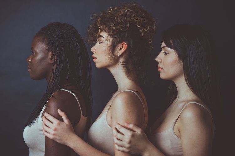 Profile view of women embracing while standing against black background