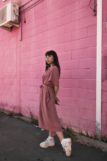Full length of woman standing against pink wall