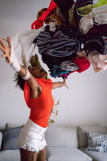 Black woman with afro hair throwing pile of clothing standing in the living room screaming
