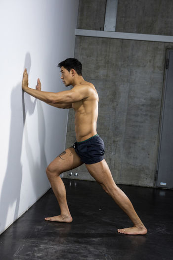 Shirtless muscular man exercising against wall