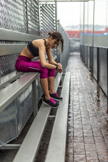 Side view full body of toned female athlete in activewear sitting on bench after outdoor workout