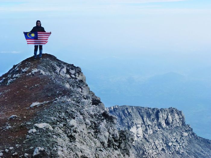 Woman with malaysian flag standing on mountain against sky