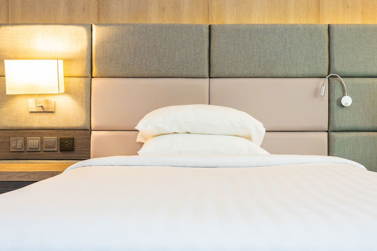 View of illuminated electric lamp by bed against wall at home
