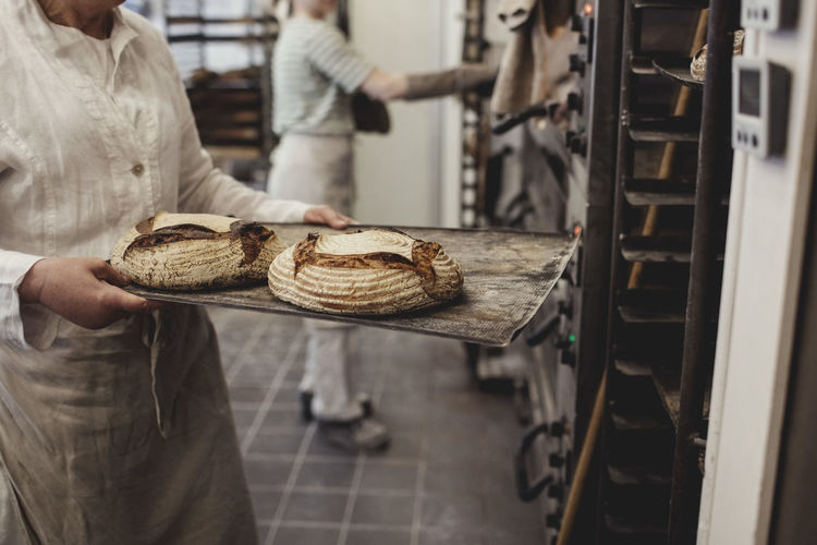 Midsection of baker keeping fresh baked breads on cooling rack at bakery