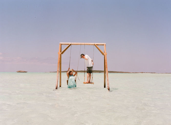 Happy couple on swing over sea against sky