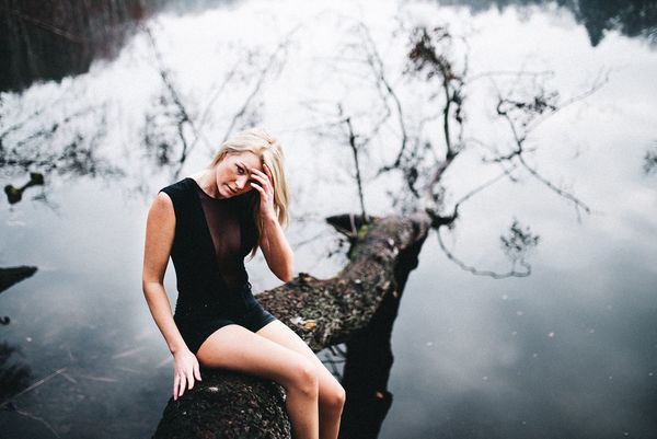 Portrait of woman with hand in hair sitting on fallen tree over lake