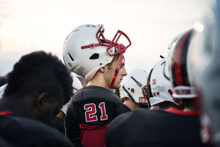 Side view teenage american football player with helmet against sky
