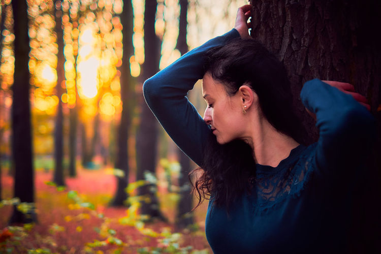Young woman standing by tree trunk in forest during autumn