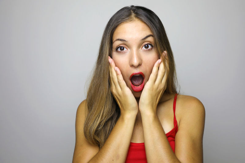 Portrait of shocked young woman against gray background