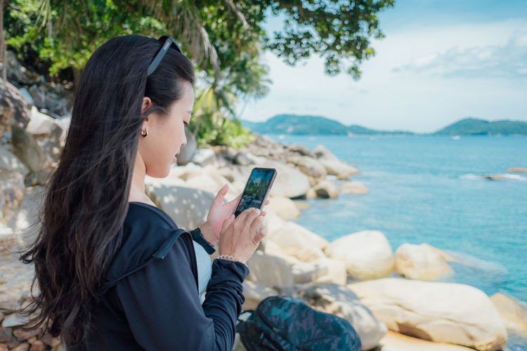 Young woman using mobile phone while sitting at beach