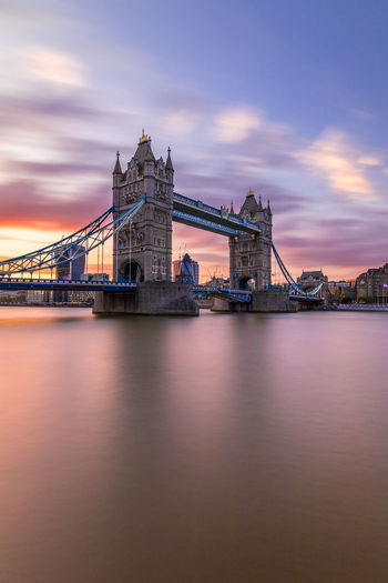 Low angle view of tower bridge over river against cloudy sky at sunset