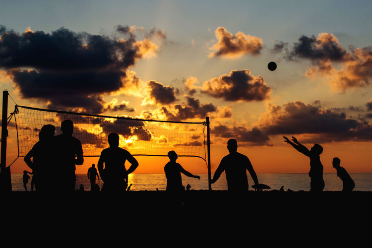 Silhouette people playing volleyball at beach against sky during sunset