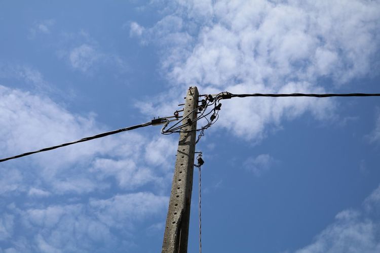 Low angle view of electricity cables on concrete pole against blue sky