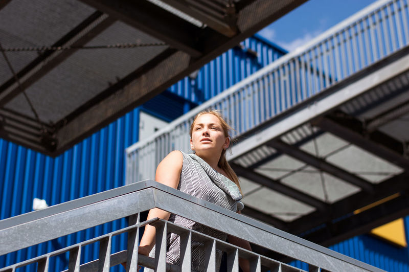Low angle view of young woman sitting on footbridge