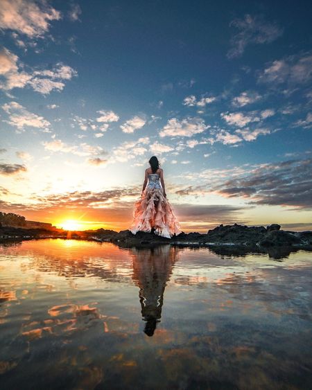 Woman standing on water against sky during sunset