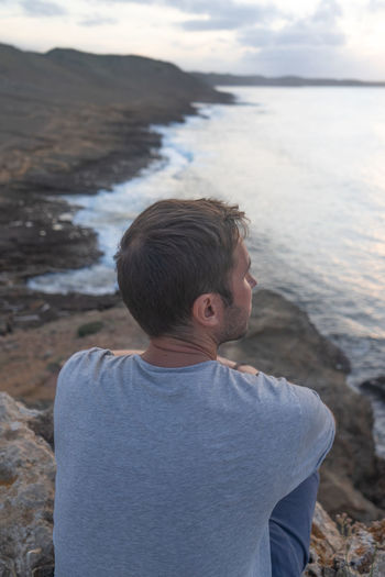 Side view of man looking at sea against sky during sunset
