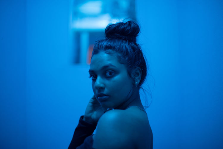 Portrait of young woman looking away against blue light 