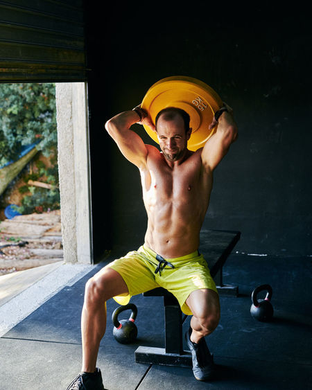 Shirtless fit young man working out in a garage with heavy disc