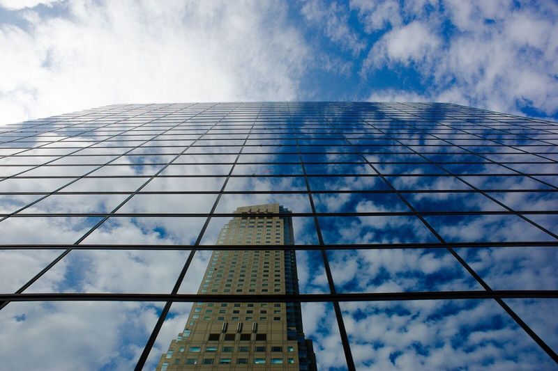 Low angle view of glass building against cloudy sky