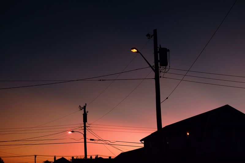 Low angle view of silhouette electricity cables and street lights against sky at sunset