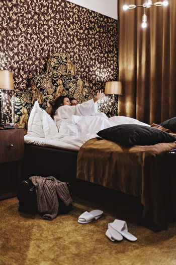 Mid adult woman taking selfie with boyfriend on bed in hotel room