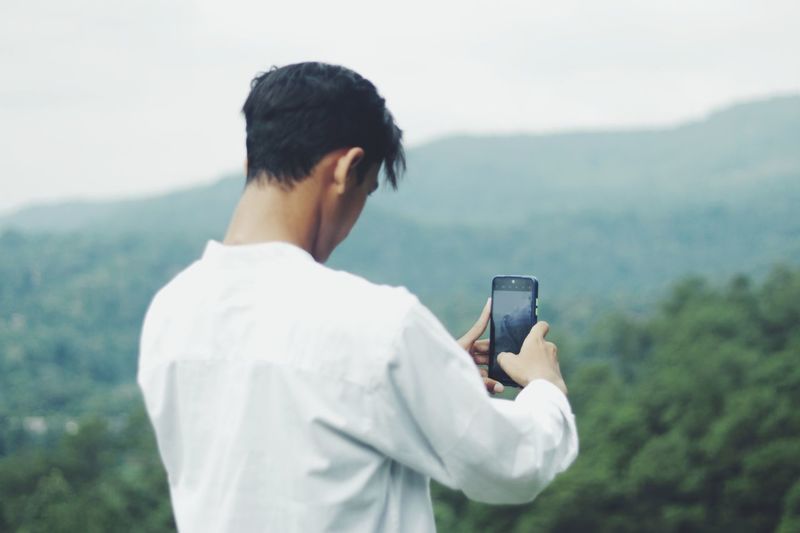 Side view of young man photographing through mobile phone