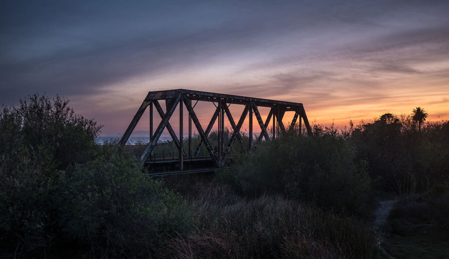 Railway bridge on field against sky during sunset