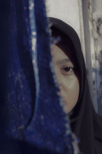 Close-up portrait of young woman in hijab by curtain