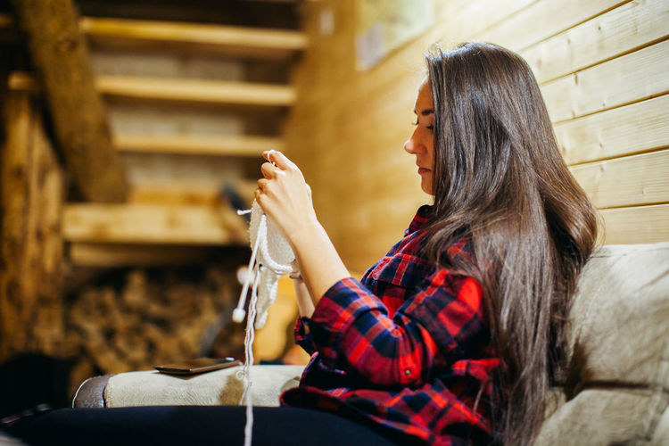 Side view of mid adult woman knitting while sitting on sofa at home