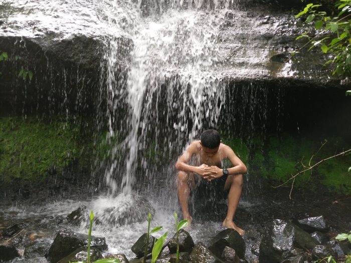 Full length of shirtless man splashing water in rocks